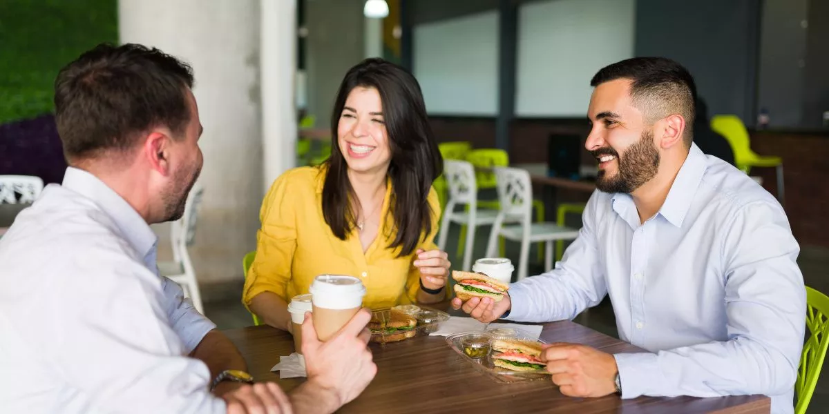 Compañeros de trabajo riendo mientras comparten el almuerzo en la oficina